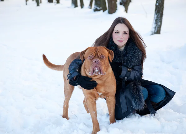 一个微笑的女人就坐在雪地里与她的狗 — 图库照片