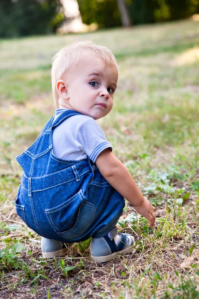 Um rapaz está à procura de algo na relva. — Fotografia de Stock
