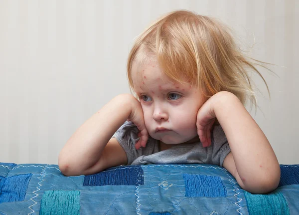 En sjuk flicka sitter nära sängen — Stockfoto