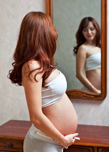 En gravid kvinna är att titta på sig själv i spegeln — Stockfoto