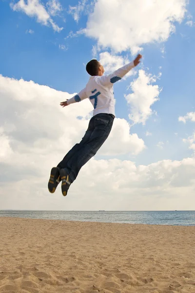 Killen hoppar in i skyen på stranden — Stockfoto