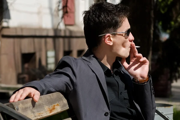Fumer jeune homme en lunettes de soleil — Photo