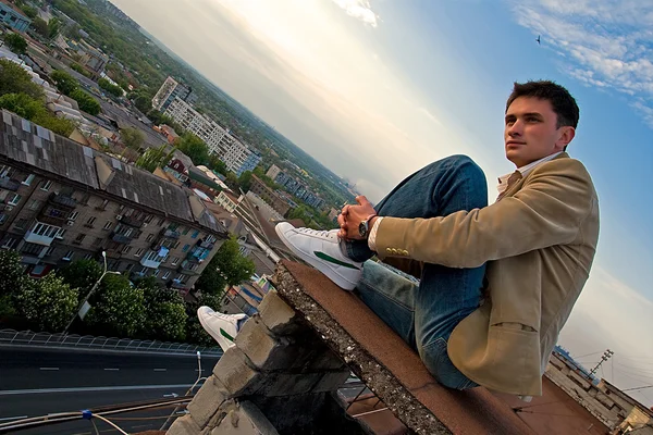 Молодой привлекательный мужчина сидит на крыше — стоковое фото