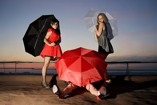 Three sexy chicks with umbrellas posing on the roof — Stock Photo, Image