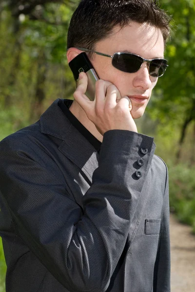 Man in sunglasses and jacket talks on cell phone — Stock Photo, Image