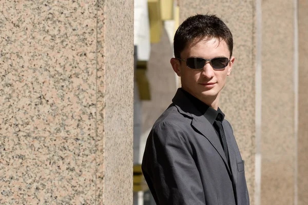 Mladý podnikatel v sluneční brýle mezi sloupci — Stock fotografie