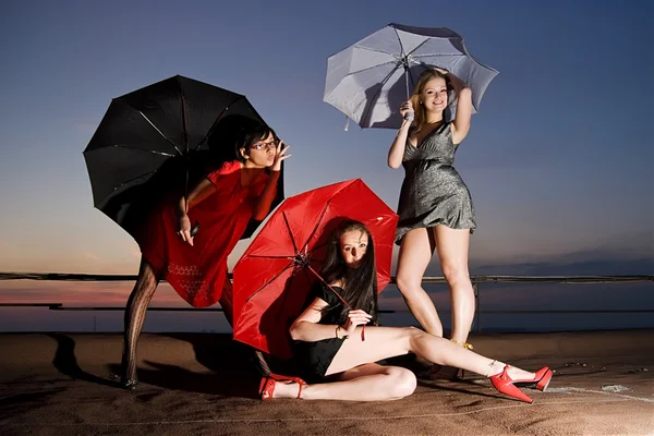 Three sexy chicks with umbrellas posing on the roof — Stock Photo, Image