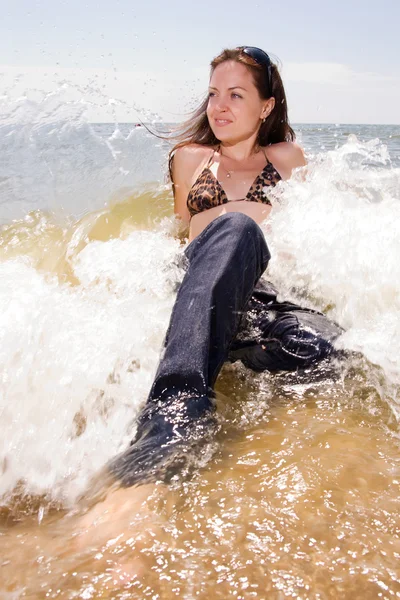 年轻的女孩坐在水溅在海滩上 — 图库照片