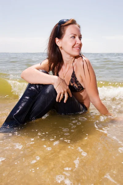 Jovem garota senta-se em respingos de água na praia — Fotografia de Stock