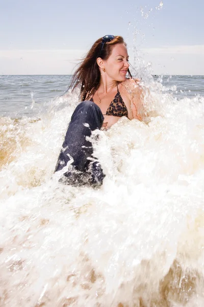 Young woman sits in water splashes at the beach