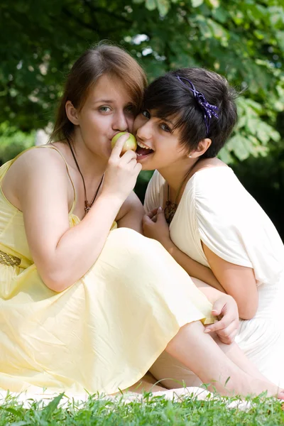 Two girls eating an apple outdoors smiling — Stock Photo, Image