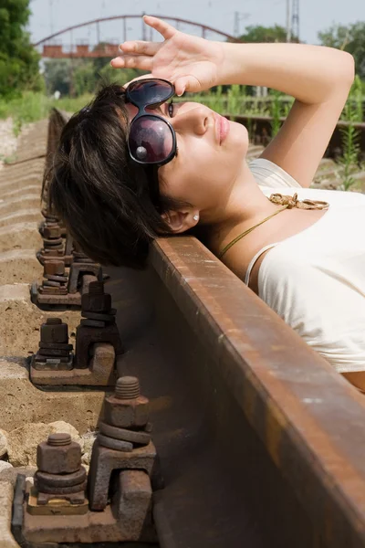 Girl in sunglasses laying carelessly on the railroad — Stock Photo, Image