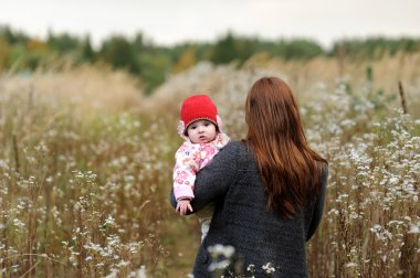 Mother with her baby girl in a meadow clipart