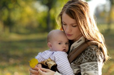 Young mother with her baby in a carrier clipart