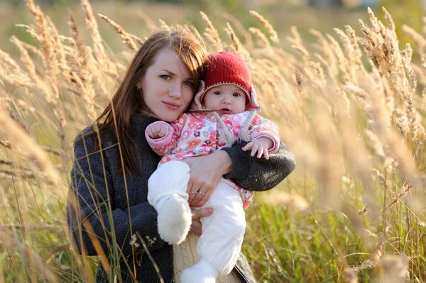 Jovem mãe segurando seu bebê em um prado — Fotografia de Stock