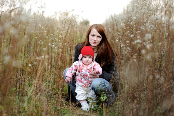 Ung mor med sin baby sitter i ett gräs — Stockfoto