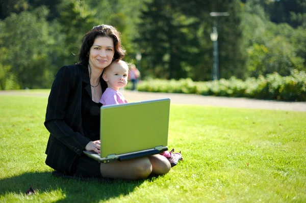 Ung dam med en bebis och en anteckningsbok i en park — Stockfoto