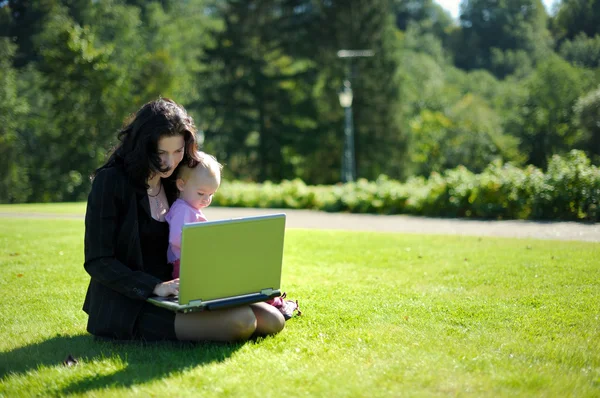 Young lady with a baby and a notebook in a park — Stock Photo, Image