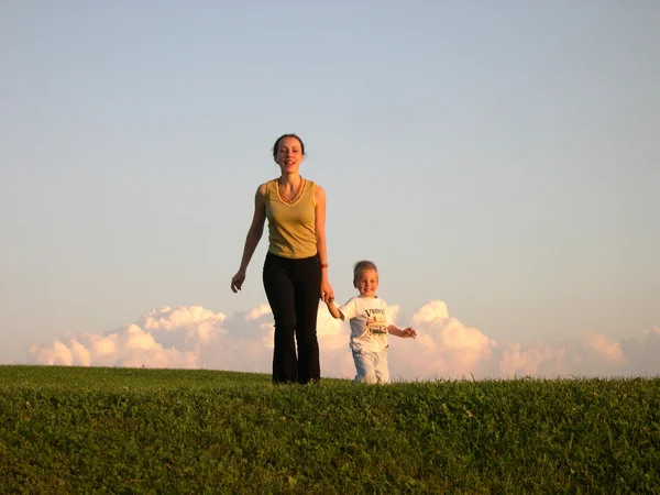 Mutter mit Sohn zu Fuß auf Sonnenuntergangswiese — Stockfoto