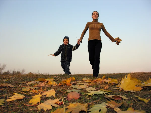 Madre que corre con el hijo en hojas de otoño — Foto de Stock