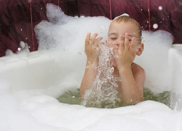 Мальчик в ванной с брызгами воды в руках — стоковое фото