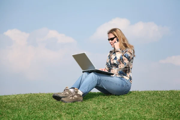 Flicka med bärbar dator och telefon på gräs — Stockfoto