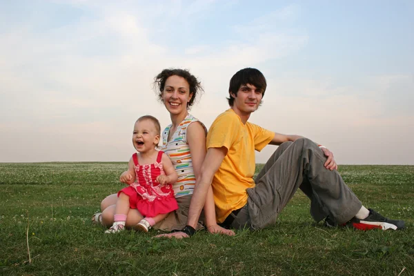 Семья с ребенком сидеть на вечернем лугу — стоковое фото
