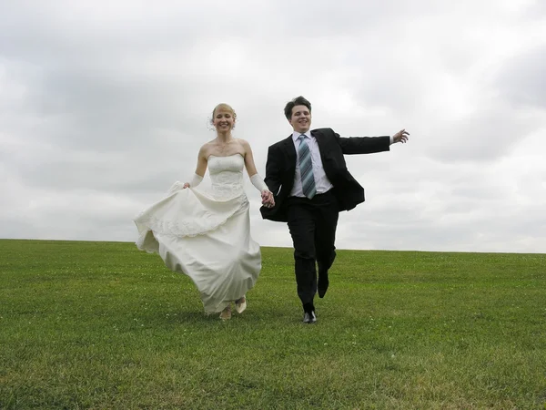 Bride and groom running on meadow — Stock Photo, Image