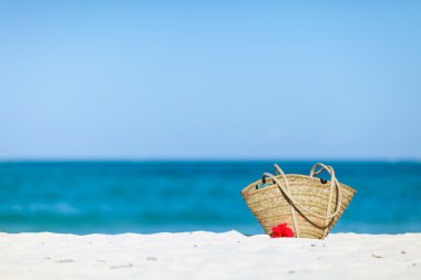Straw beach bag on exotic white sand beach clipart