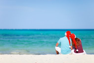 Romantic couple in Santa hats sitting on tropical beach clipart