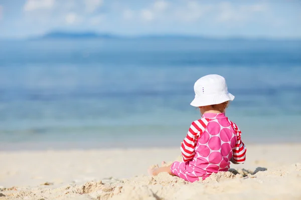蹒跚学步的女孩坐在白色的沙滩上 — 图库照片