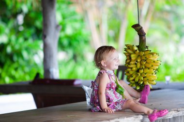 peuter meisje buitenshuis met bos van bananen