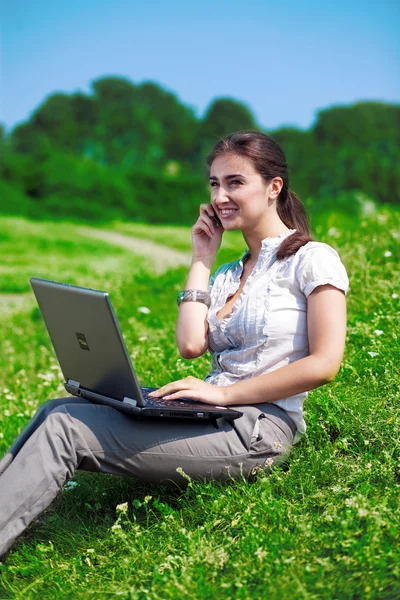 Mooie vrouw met telefoon en notebook op gras — Stockfoto