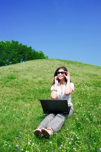 Mujer con portátil y teléfono sentarse en la colina — Foto de Stock