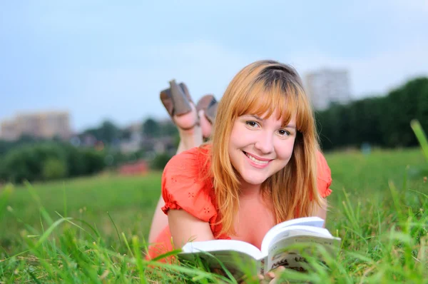 Jeune femme souriante couchée sur la prairie avec un livre — Photo