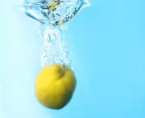 Limone fresco caduto in acqua con spruzzata isolata sul blu — Foto Stock