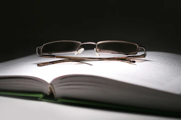 A nyitott könyv és egy sötét vissza szemüveg — Stock Fotó