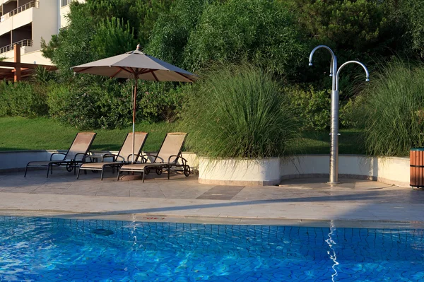 Camas de sol, guarda-sóis e chuveiro perto da piscina . — Fotografia de Stock