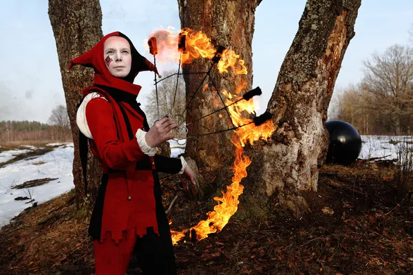 Artistic woman in a suit of fire-clown holds a fiery fan posing — Stock Photo, Image