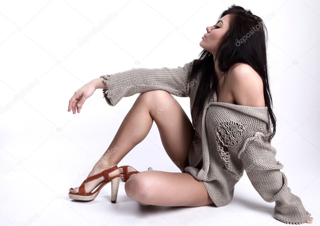 Siting beautiful young brunette in a woollen sweater on a grey b
