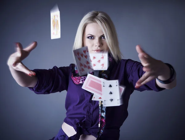 Blonde in violet op een grijze achtergrond verstrooit speelkaarten. — Stockfoto