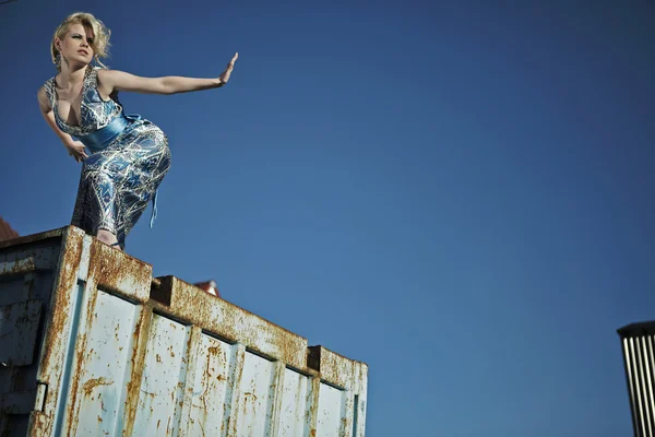 Elegante dama en un vestido de cóctel contra el viejo contenedor oxidado . — Foto de Stock