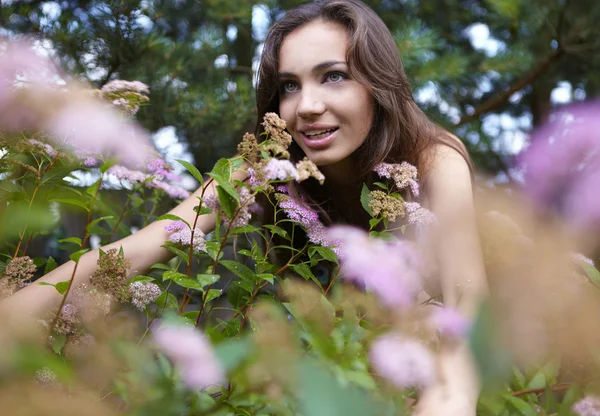 Vacker flicka sitter bland bush blommor — Stockfoto