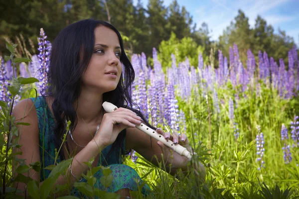 Attractive girl with a flute sitting in a summer field. — Stock Photo, Image