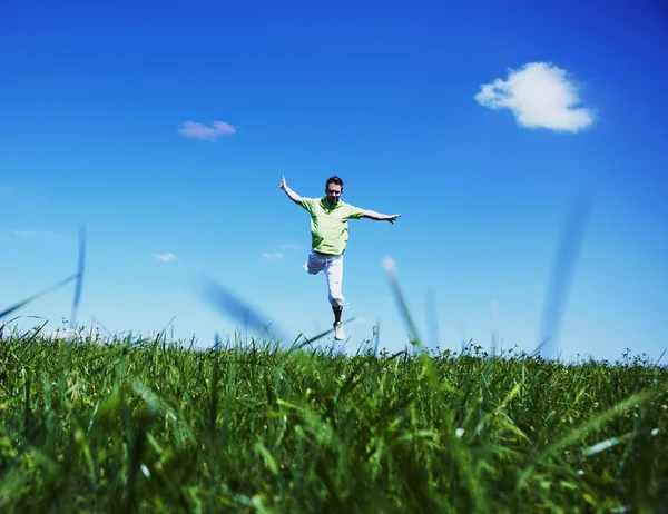 Skaczący w górze facet w zielonej koszuli przeciw błękitne niebo. — Zdjęcie stockowe