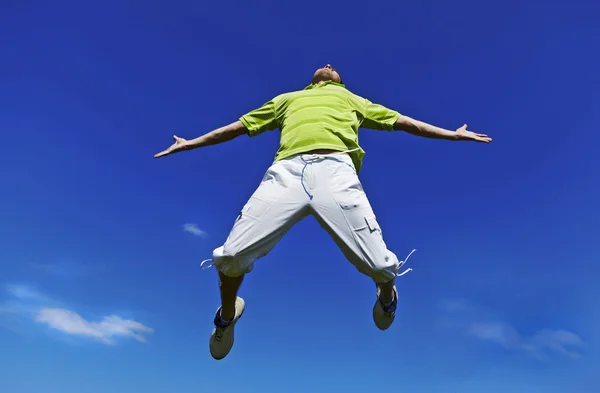 Skaczący w górze facet w zielonej koszuli przeciw błękitne niebo. — Zdjęcie stockowe