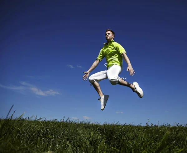 Mann springt in grünem Hemd gegen blauen Himmel auf. — Stockfoto