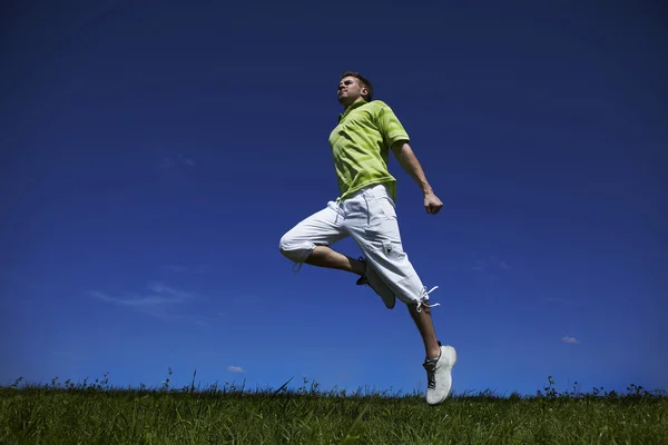 Springen man in een groen shirt tegen blauwe hemel. — Stockfoto