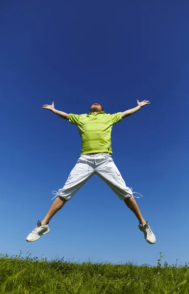 Прыгающий парень в зеленой рубашке на фоне голубого неба . — стоковое фото