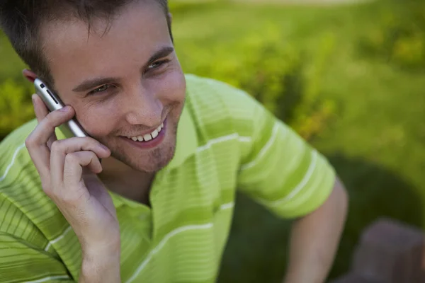 stock image Cheerful guy in a green vest speaks by phone.